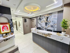 Ein Empfangsbereich mit Marmor-Theke, Deckenventilator und einer Wand mit Hinweisen zu Check-in- und Check-out-Zeiten.