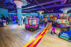Eine Indoor-Spielhalle mit verschiedenen Spielautomaten, Holzboden und einem farbenfrohen Streifenmuster.