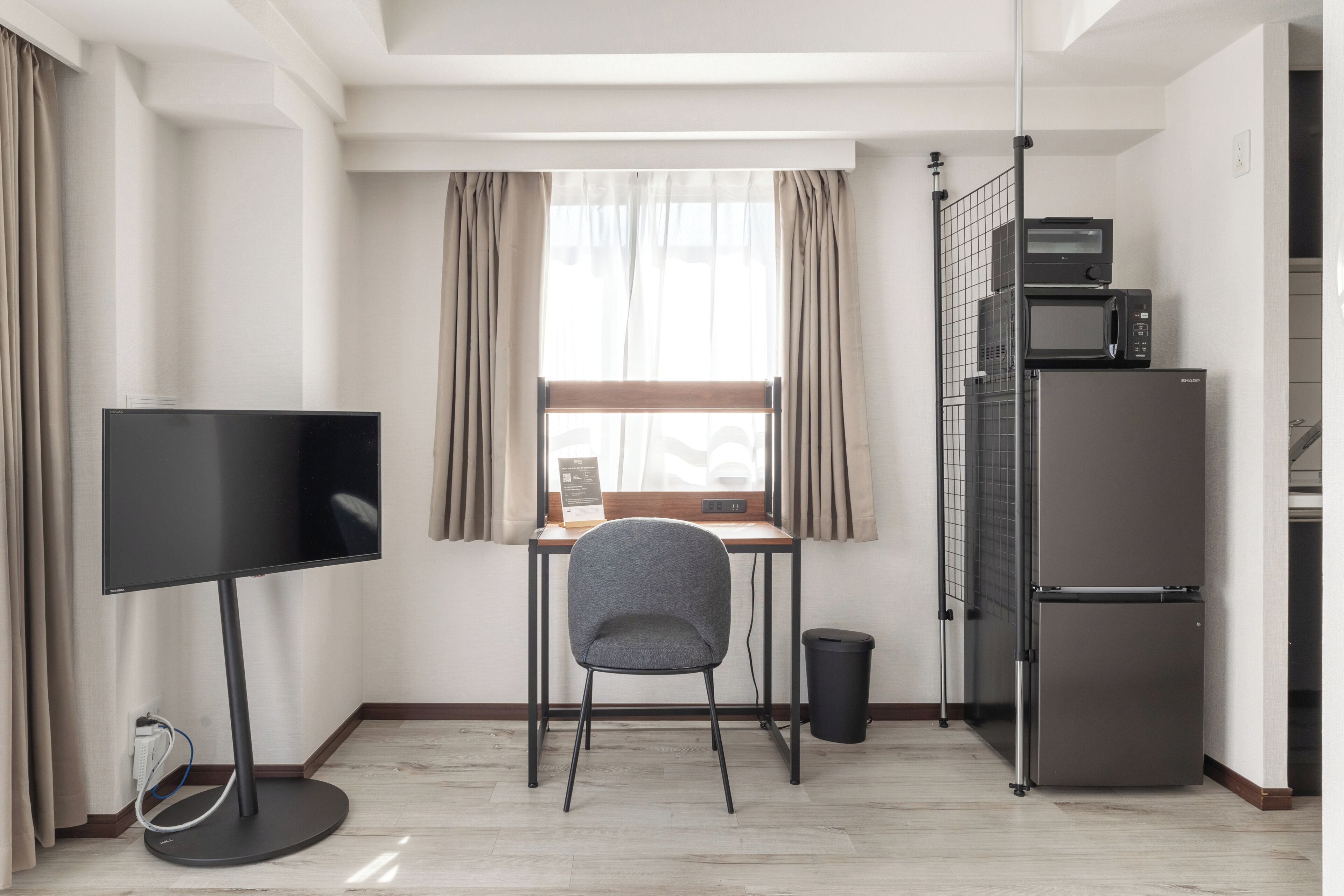 A compact room with a desk, chair, flat-screen TV, microwave, and refrigerator.