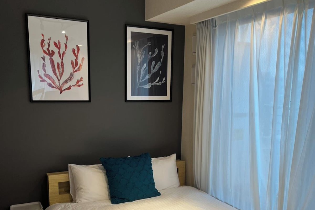 A hotel room with a bed, a nightstand, a trash bin, and two framed artworks on the wall.