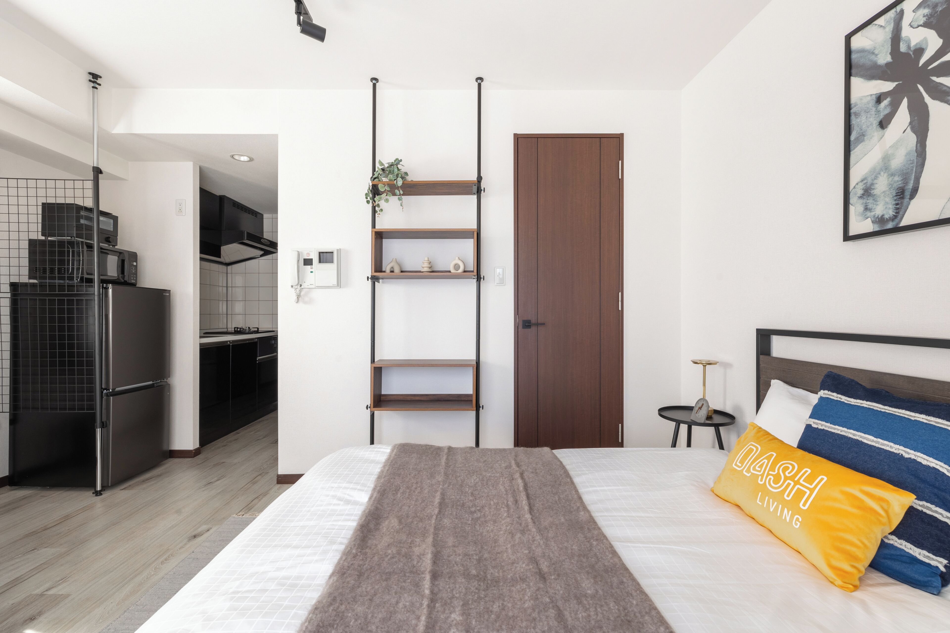 A modern bedroom with a bed, a bedside table, a nightstand, a wardrobe, a kitchen area, and a bathroom.
