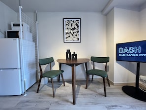 A modern kitchen with a white refrigerator, a microwave, and a coffee machine. There is a dining table with two chairs and a framed artwork on the wall. - Dash Living Ryogoku (Sumida City)