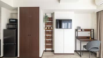 A compact kitchen with a microwave, refrigerator, and a TV mounted above a desk with a chair.