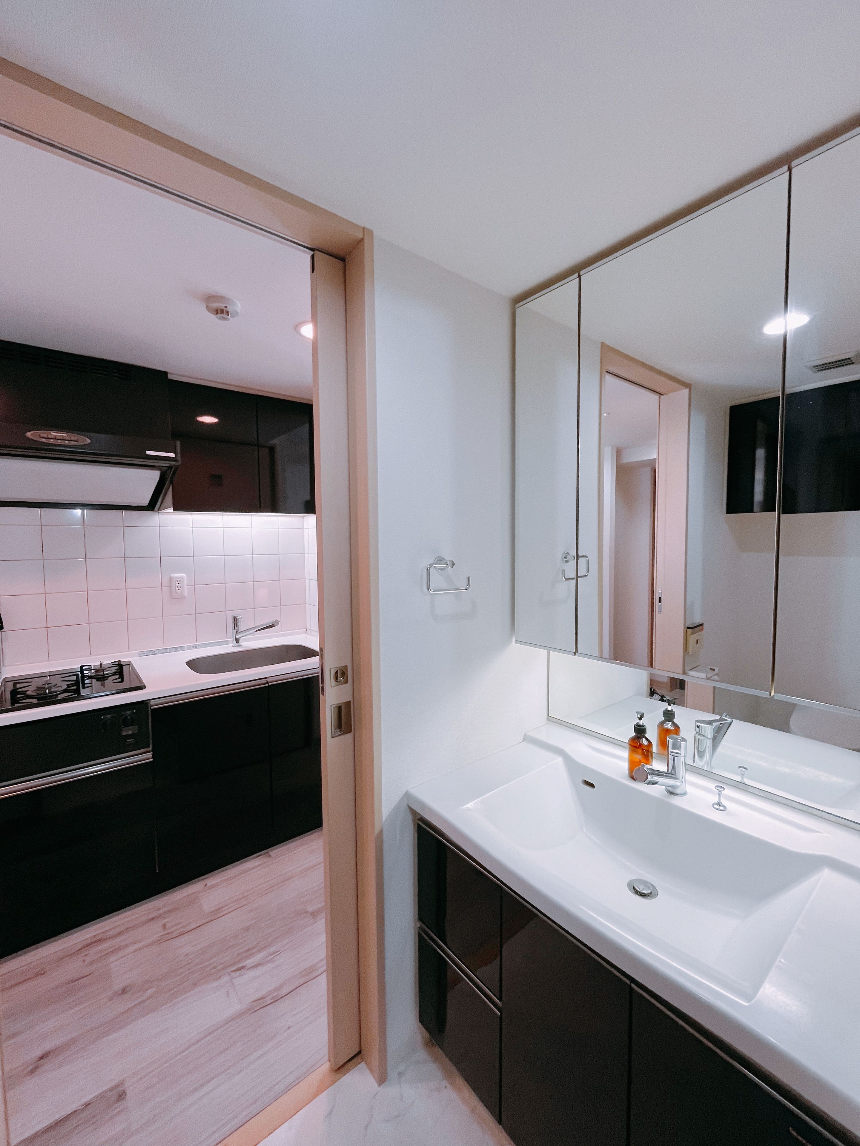 A modern bathroom with a large mirror, a white sink, and a dark-toned cabinet.