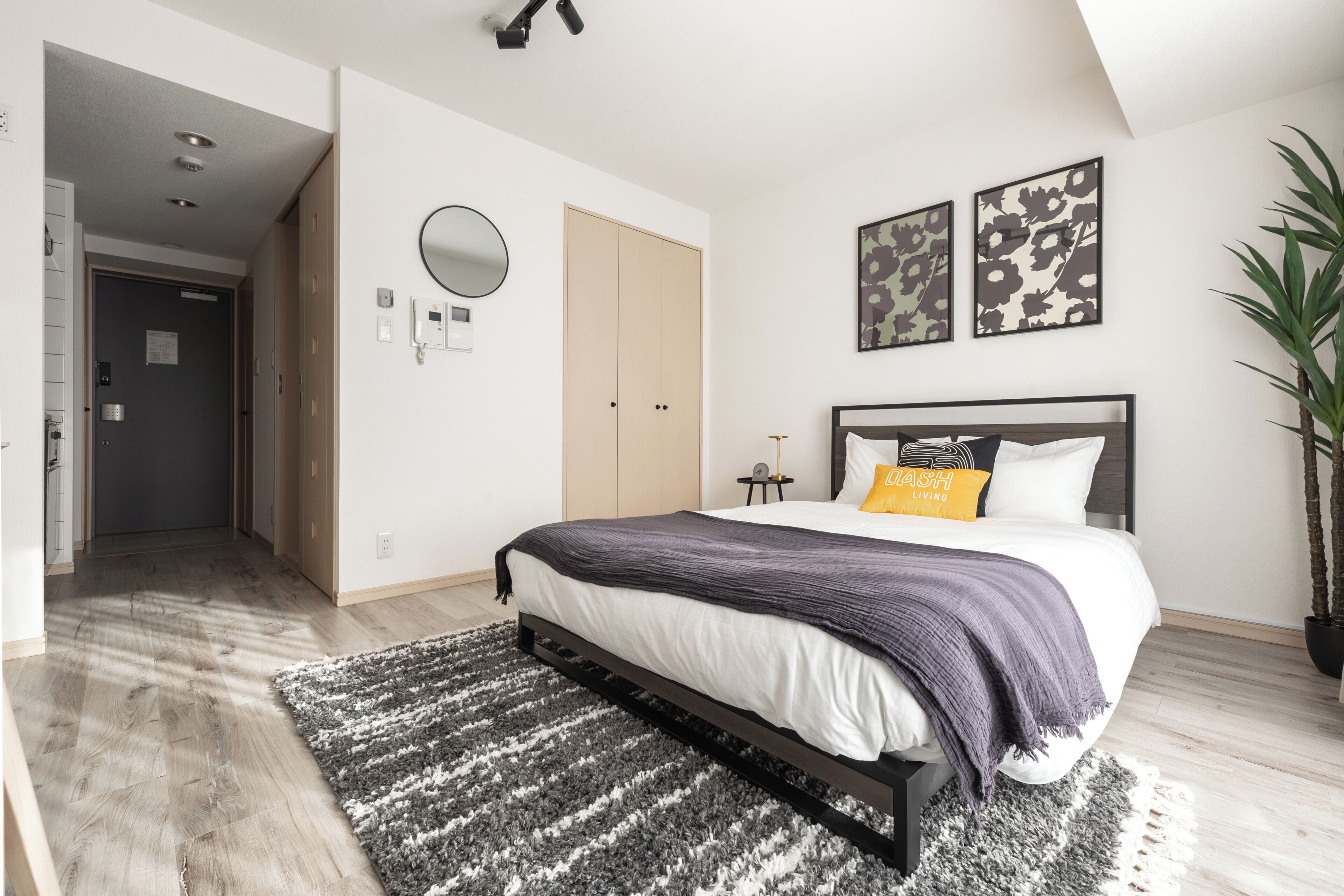 A bedroom with a bed, a bedside table, a mirror, and a potted plant.