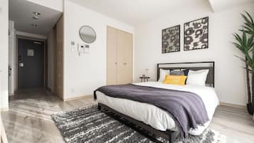 A bedroom with a bed, a bedside table, a mirror, and a potted plant.