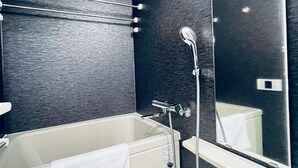 A modern bathroom with a bathtub, a shower, a mirror, and a wall-mounted air vent. - Dash Living Ryogoku (Sumida City)
