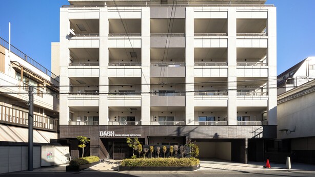 A multi-story building with balconies, a sign reading 'DASH DASH LIVING ITOGOKU,' and a small garden area in front. - Dash Living Ryogoku (Sumida City)
