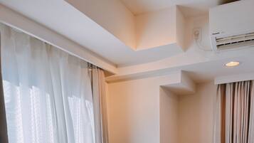 A hotel room with a round dining table, two chairs, a flat-screen TV, and an air conditioning unit on the wall.
