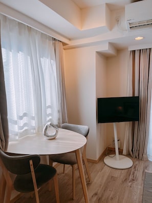 A hotel room with a round dining table, two chairs, a flat-screen TV, and an air conditioning unit on the wall. - Dash Living Ryogoku (Sumida City)