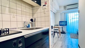 A modern kitchen with a dishwasher, a sink, and a stove. There is a dining area with a table and chairs, and a television displaying 'DASH LIVING IYOKU'. - Dash Living Ryogoku (Sumida City)