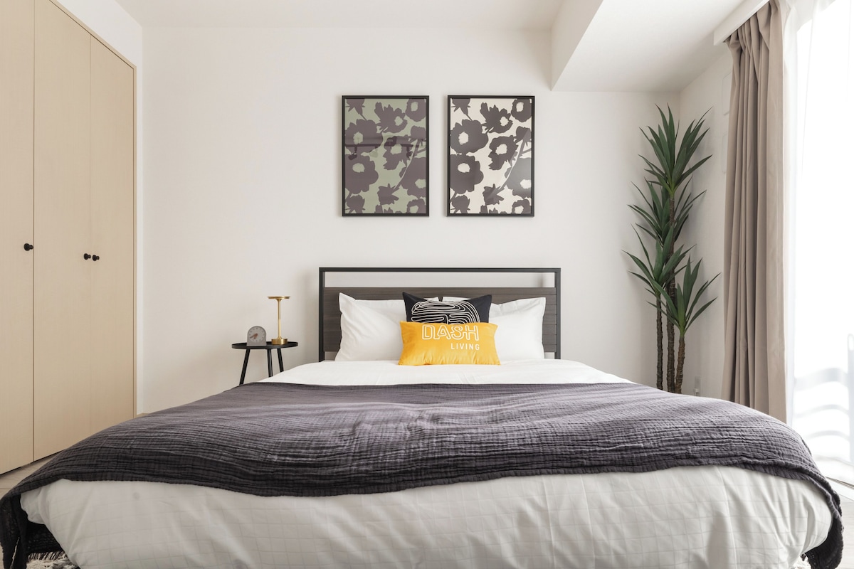 A bedroom with a bed, a nightstand, a potted plant, and two wall-mounted artworks.