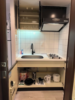 A compact kitchen with a sink, stove, and storage cabinets. - Dash Living Ryogoku (Sumida City)