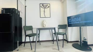 Quarto moderno com mesa de jantar, duas cadeiras, geladeira preta, TV de tela plana e uma obra de arte emoldurada na parede.