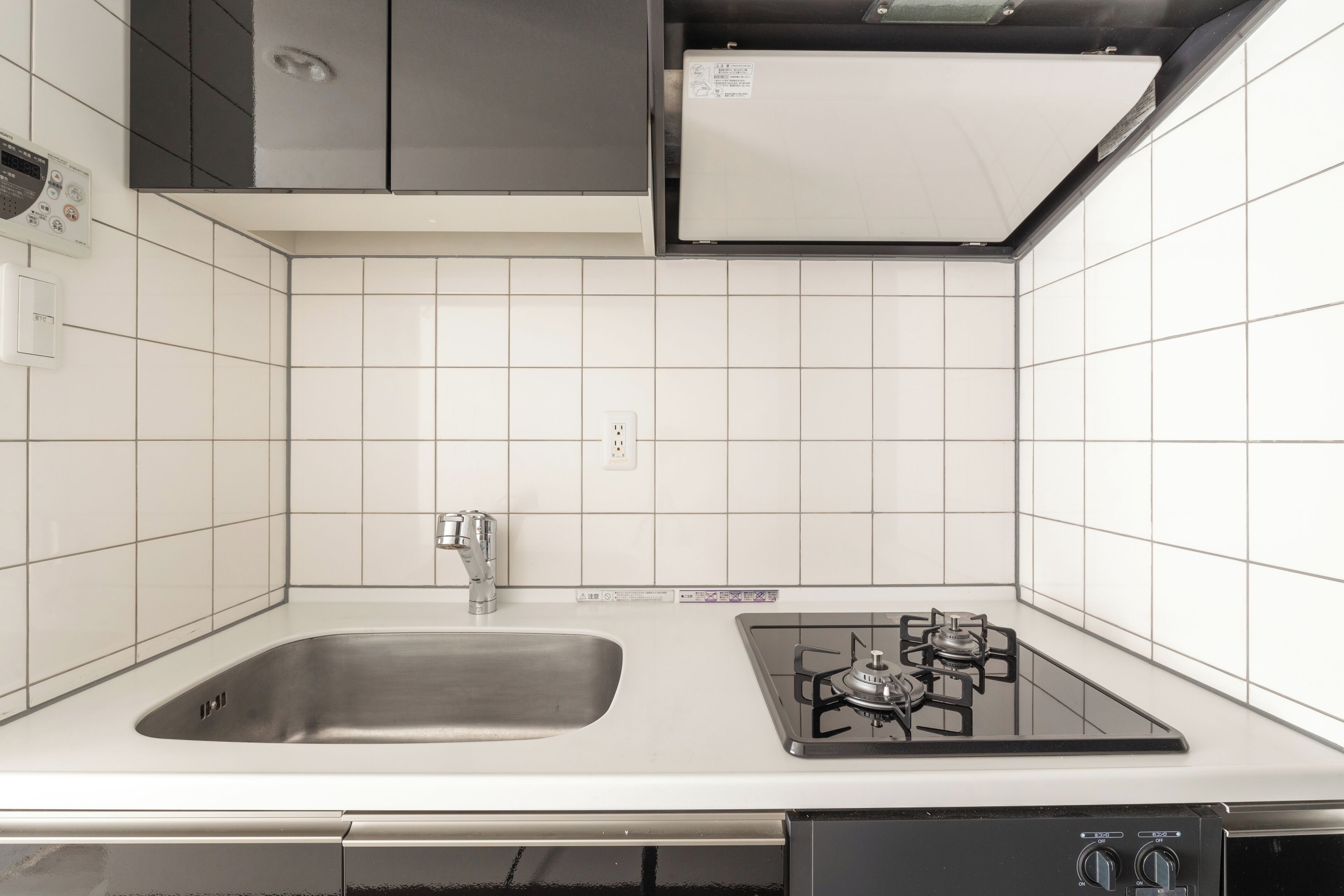 A kitchen with white tiles, a stainless steel sink, a gas stove, and a dishwasher.