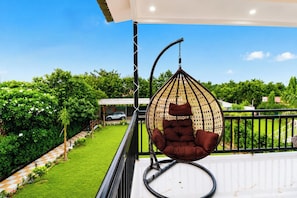 A hanging chair on a balcony with a view of a well-maintained garden and a parked car in the background. - 4 Bedroom Farmhouse With Private Pool In Noida (Nodia)