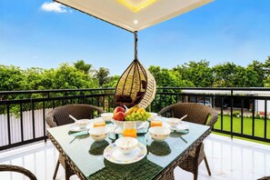 A balcony with wicker furniture, a hanging chair, and a table set with bowls, fruits, and juice. - 4 Bedroom Farmhouse With Private Pool In Noida (Nodia)