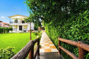 A pathway leading to a building with a balcony, surrounded by greenery. - 4 Bedroom Farmhouse With Private Pool In Noida (Nodia)
