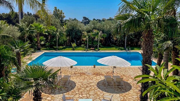 Ein Pool mit zwei Sonnenschirmen, Liegestühlen und einer Steinterrasse.