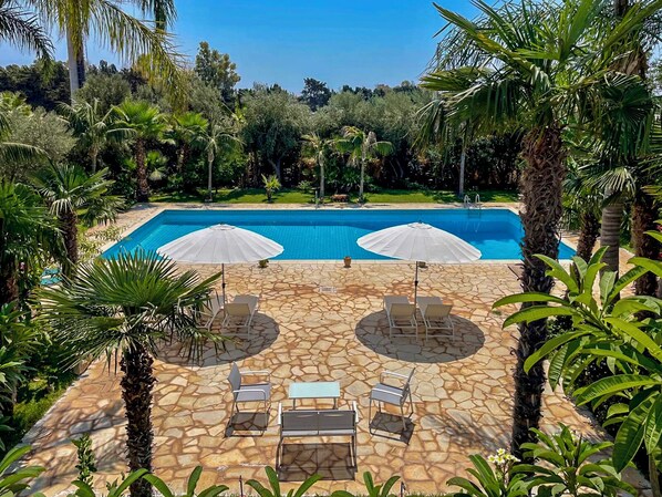 Ein Pool mit zwei Sonnenschirmen, Liegestühlen und einer Steinterrasse.