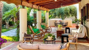 Eine Terrasse im Freien mit Korbmöbeln, einem Deckenventilator und Topfpflanzen.