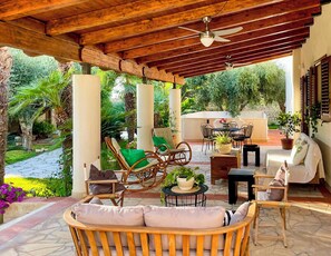 Eine Terrasse im Freien mit Korbmöbeln, einem Deckenventilator und Topfpflanzen.