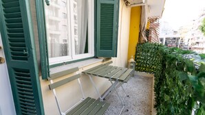 Un balcon avec une table en métal vert et deux bancs, une porte jaune et une haie.