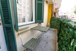 Ein Balkon mit einem grünen Metalltisch und zwei Bänken, einer gelben Tür und einer Hecke.