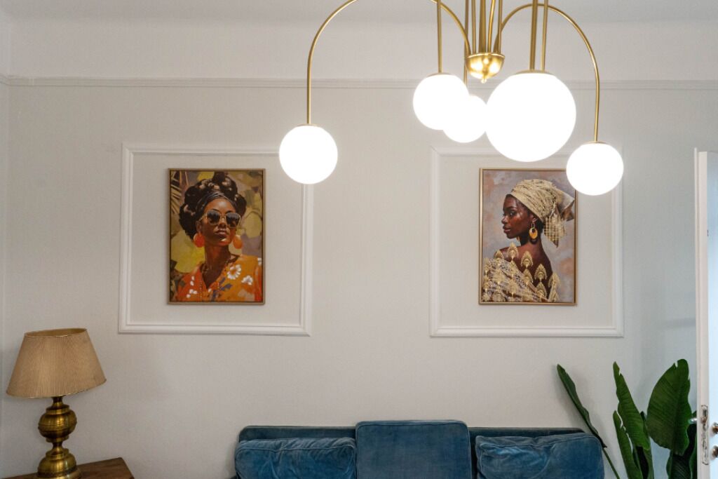 A room with a blue sofa, two framed artworks on the wall, a gold lamp, and a hanging light fixture.