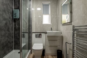 Een badkamer met een douchecabine van glas, een wit toilet, een wastafel met spiegel en een handdoekrek.