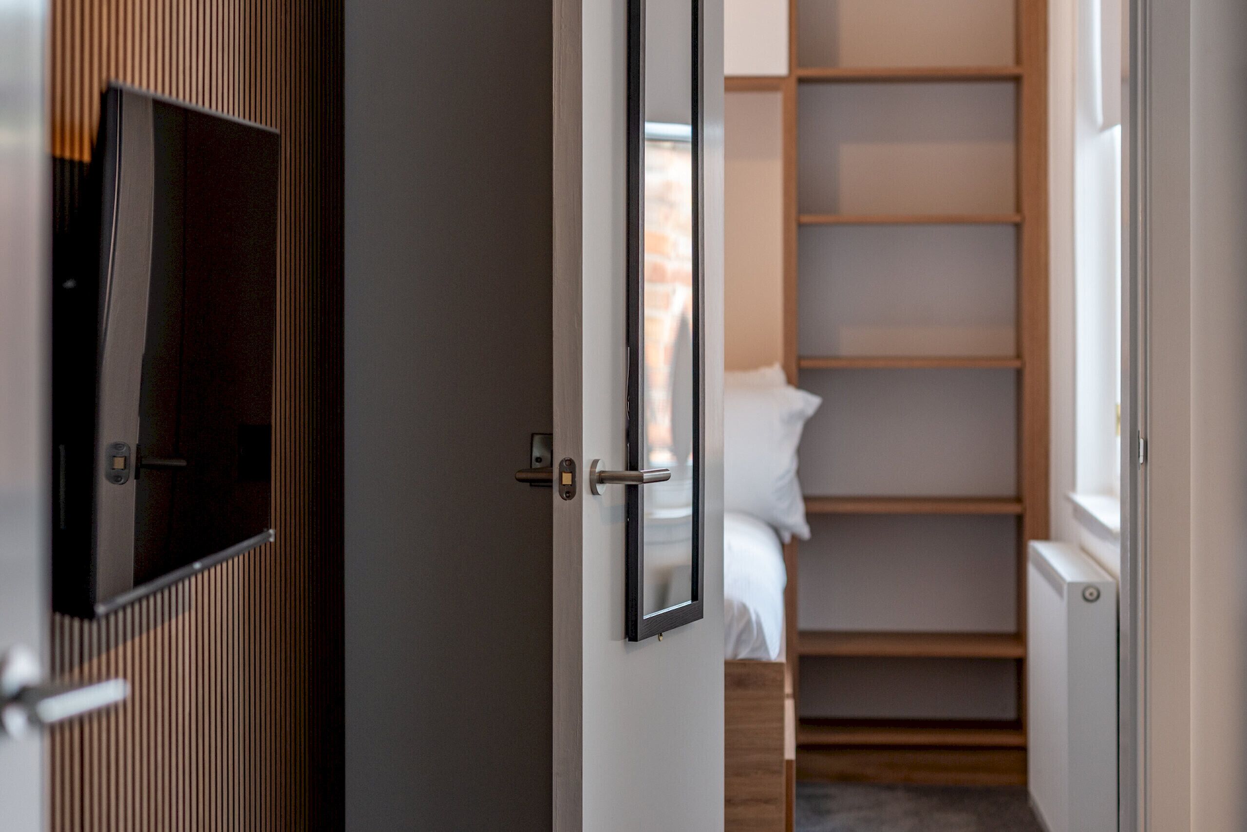 Hotellihuone, jossa on puinen vaatekaappi, valkoisilla lakanoilla varustettu sänky ja seinälle asennettu televisio.