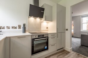 A modern kitchen with a built-in oven, a microwave, and a range hood. - Marine Place | Flat 5 (St Andrews)