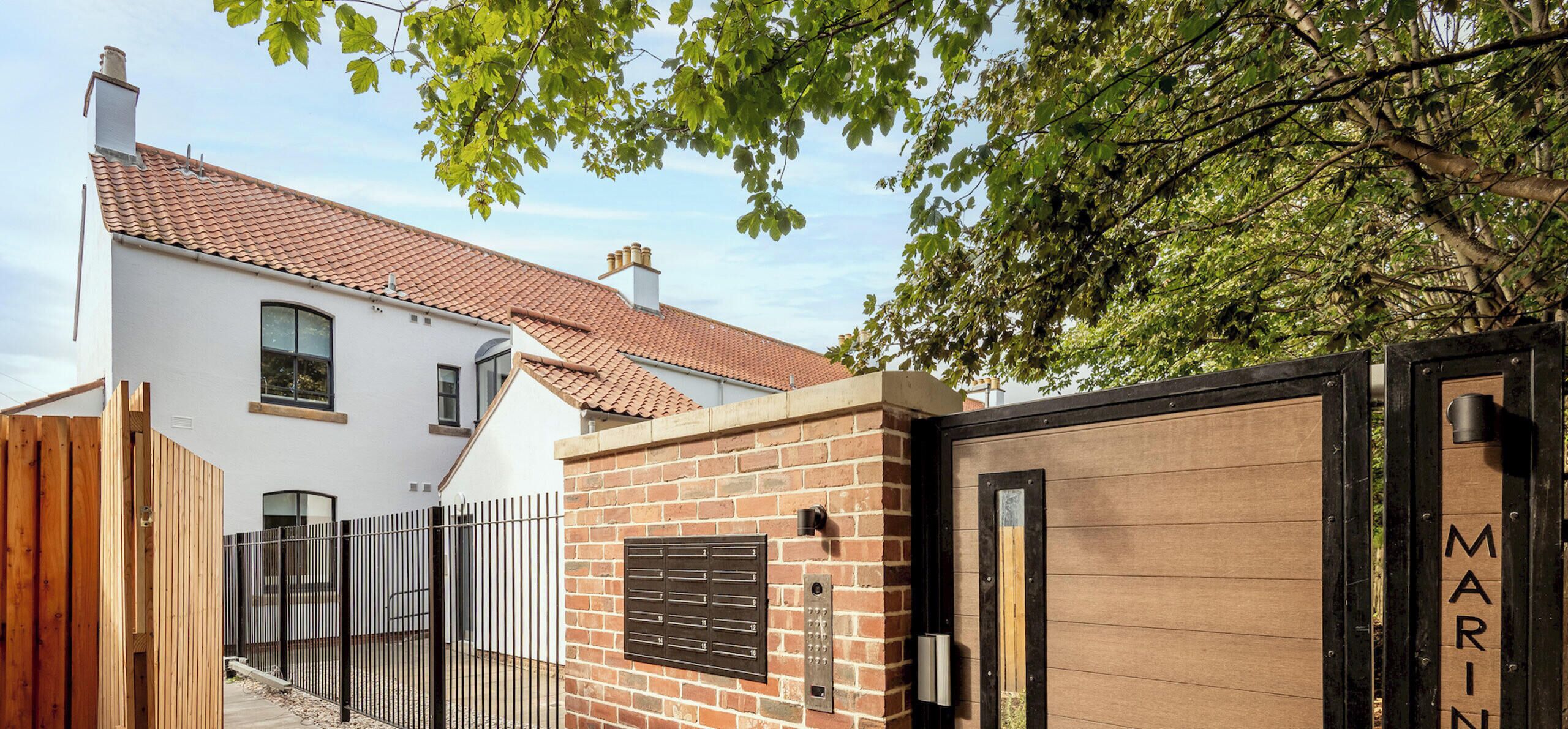 A residential building with a red-tiled roof, a brick wall, and a wooden gate.