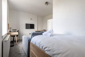Ein Schlafzimmer mit einem Bett, einem Schreibtisch mit Stuhl, einem Fernseher an der Wand und einem Fenster.