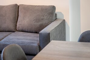 Ein Ecksofa mit hellem Kissen, einem Holztisch und einer weißen Säule.
