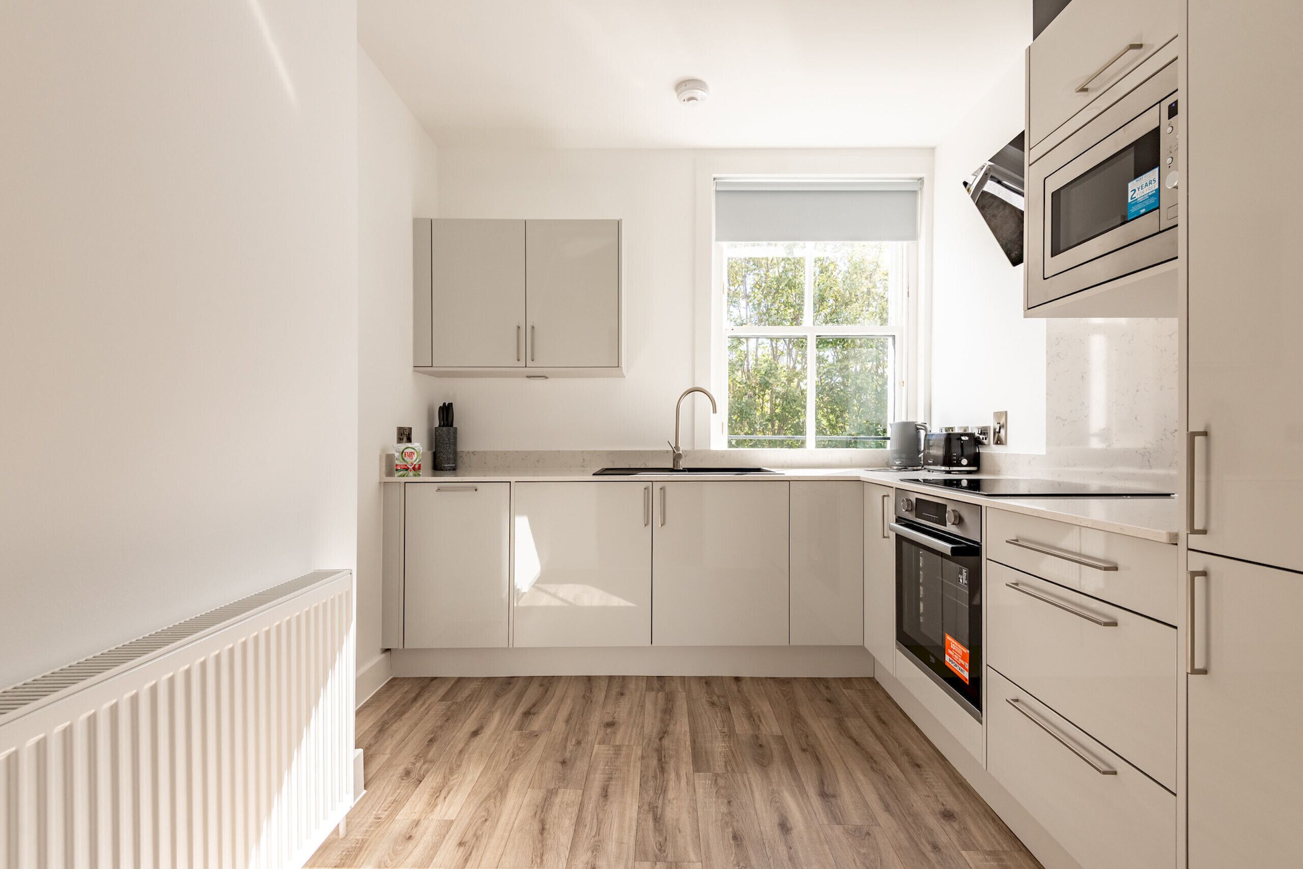 Una cocina moderna con armarios blancos, una ventana y un horno empotrado.
