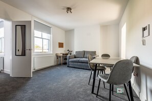 Ett modernt rum med ett matbord, stolar, en soffa, ett element och en dörr.