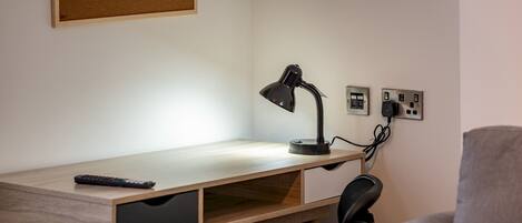 A desk with a lamp, a remote control, and a power outlet.