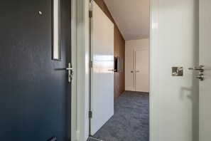 Ein Flur mit einer dunklen Tür, einer weißen Tür und einer Wand aus Holzverkleidung.