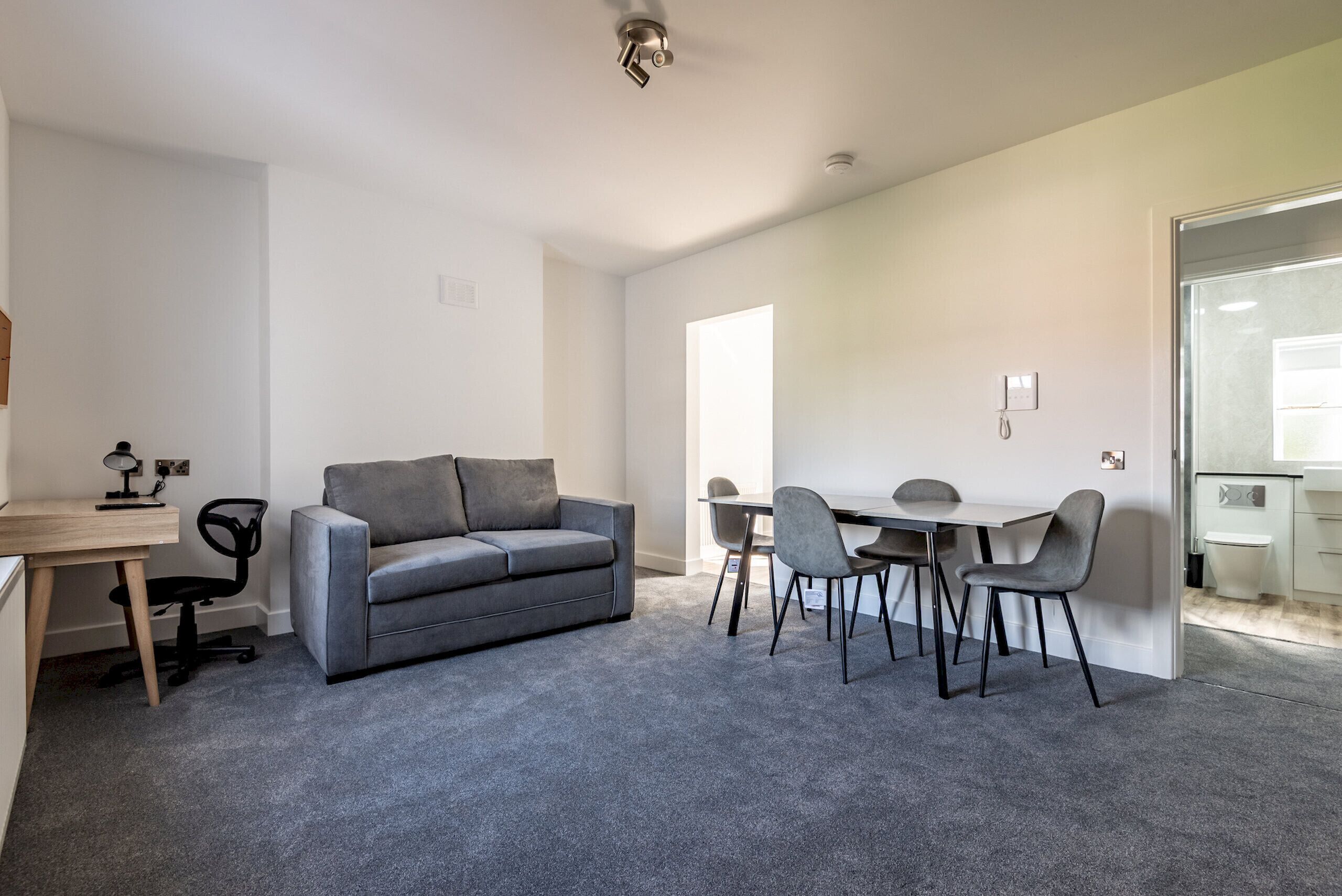 Et moderne værelse med en grå sofa, et træskrivebord og et spisebord med stole.
