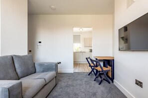 Ein modernes Wohnzimmer mit einem grauen Sofa, einem Essbereich mit Holztisch und -stühlen sowie einer Küche im Hintergrund.