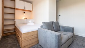 Ein Schlafzimmer mit einem Bett, einem grauen Sofa, einem Holzschrank und einer Wandleuchte.