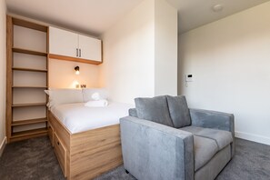 Ein Schlafzimmer mit einem Bett, einem grauen Sofa, einem Holzschrank und einer Wandleuchte.