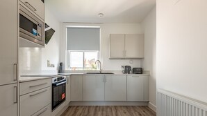 Eine Küche mit weißen Schränken, einer Mikrowelle, einem Backofen und einem Fenster.