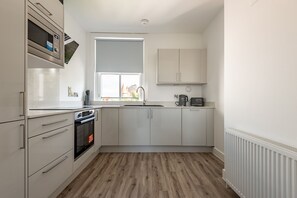 Eine Küche mit weißen Schränken, einer Mikrowelle, einem Backofen und einem Fenster.