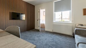 Une chambre moderne avec un téléviseur à écran plat fixé sur un mur recouvert de panneaux en bois, une grande fenêtre offrant une belle vue, une moquette grise et un canapé gris.