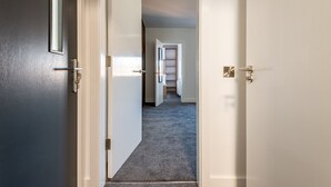 Un couloir doté d’un sol recouvert de moquette, d’une porte avec une poignée et d’un chambranle de porte blanc.