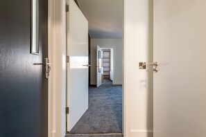 A hallway with a carpeted floor, a door with a handle, and a white door frame. - Marine Place | Flat 11 (St Andrews)
