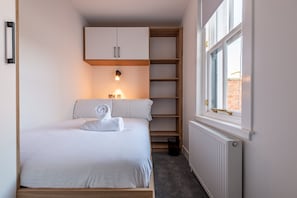 A bedroom with a bed, a built-in wardrobe, a radiator, and a window with a view. - Marine Place | Flat 9 (St Andrews)
