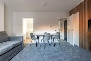 A modern living room with a grey sofa, a dining table with four chairs, and a grey carpet. - Marine Place | Flat 9 (St Andrews)